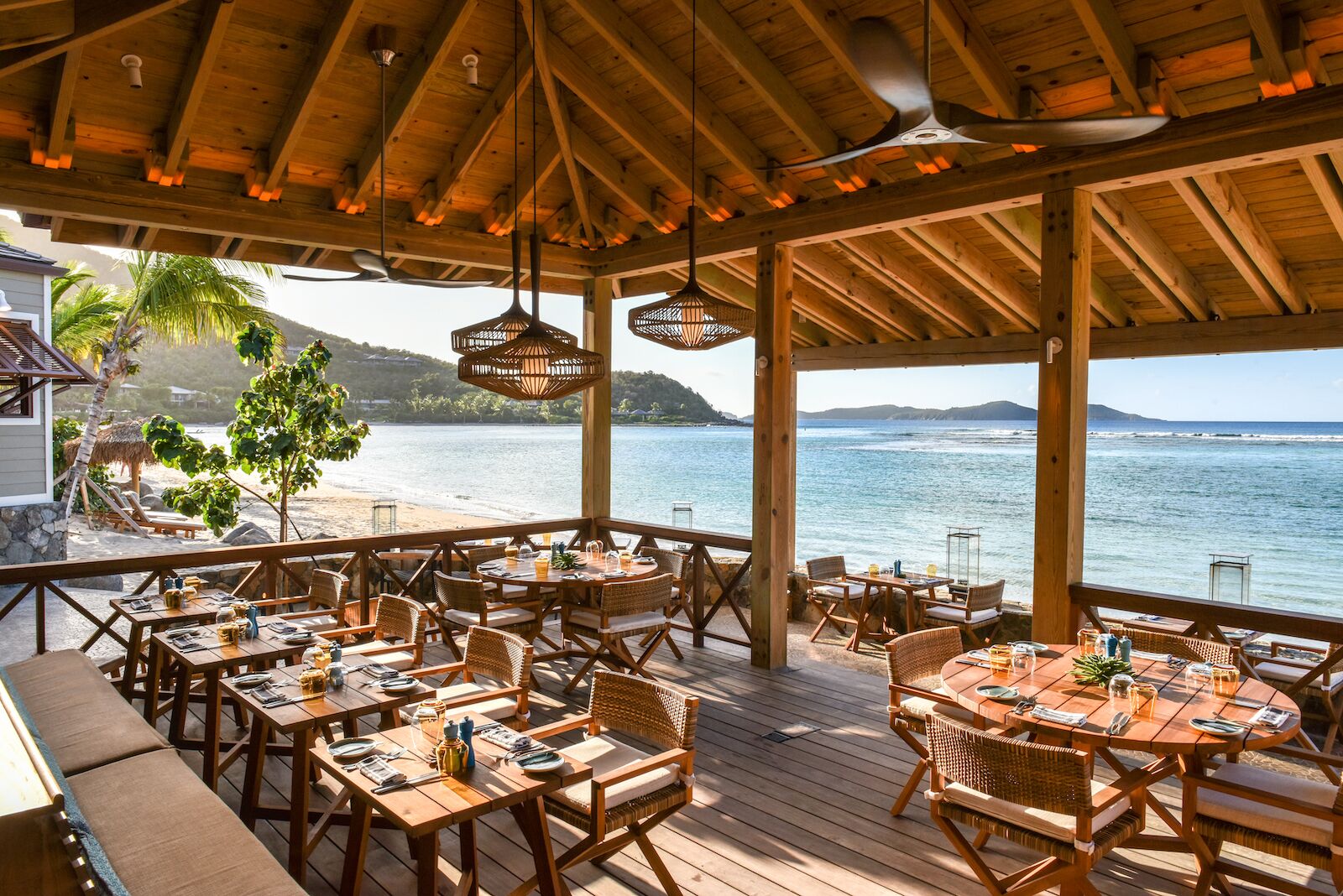 interior of open air Rosewood Little Dix Bay Reef House restaurant with ocean view and empty chairs and tables