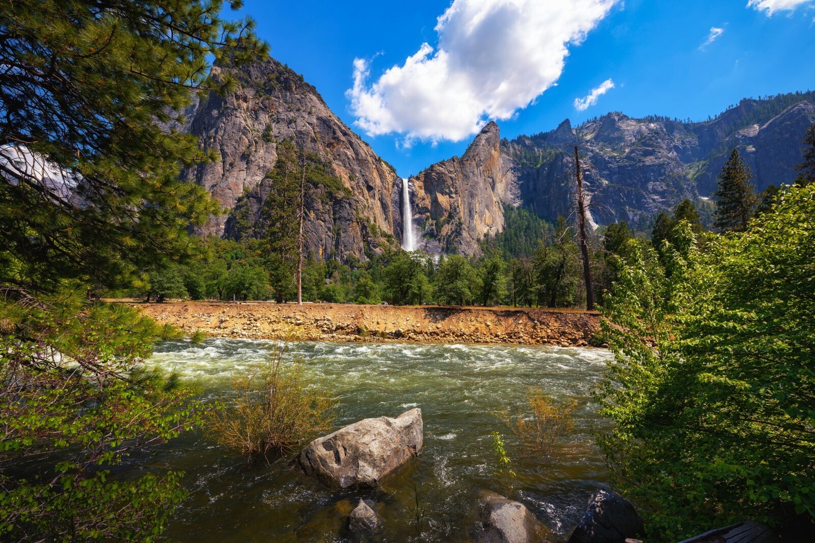 Bridalveil Fall cascading into Yosemite Valley with the Merced River in the foreground in Yosemite National Park, California