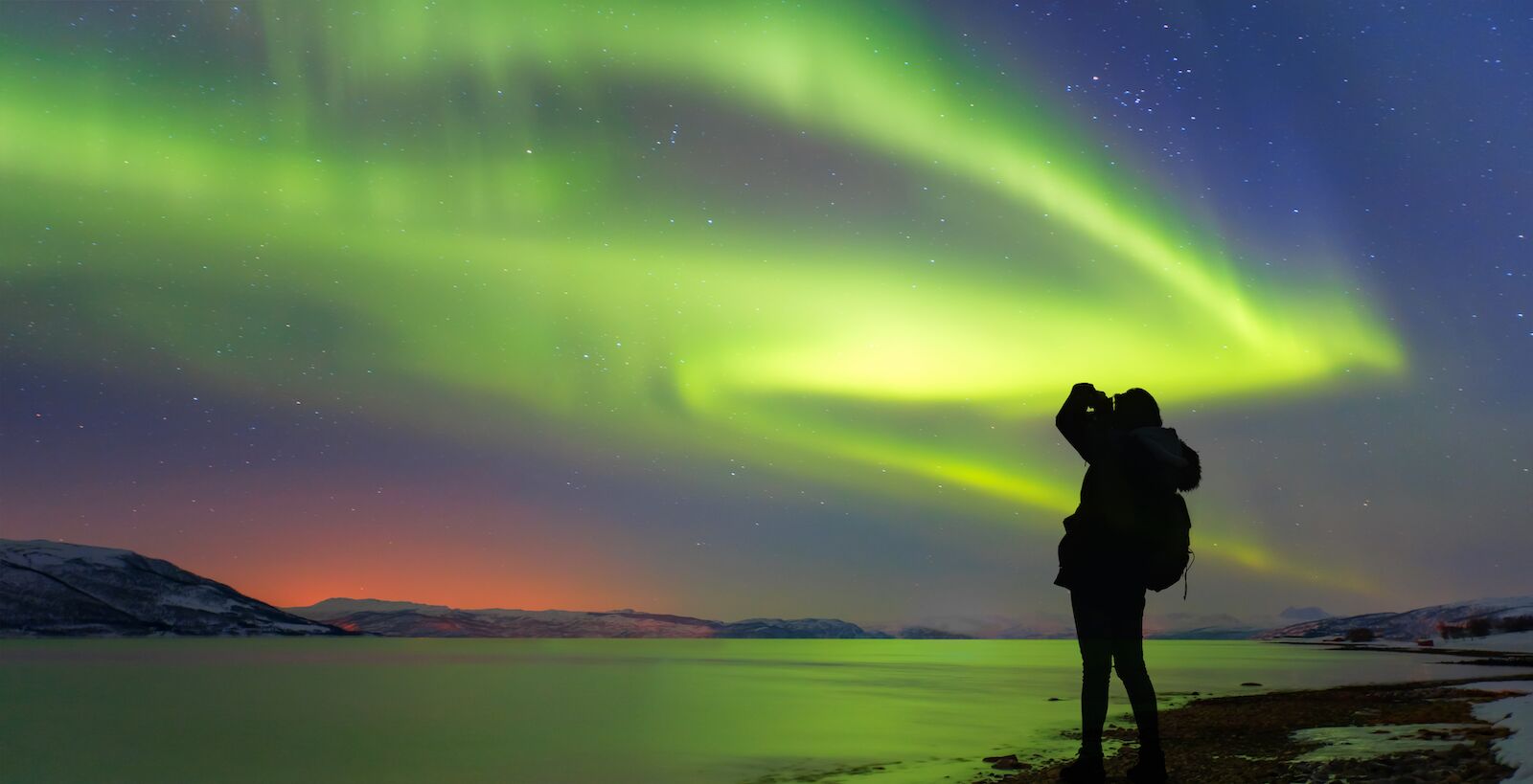 Silhouette of female photographer take a photograph at aurora borealis - Northern lights in the sky