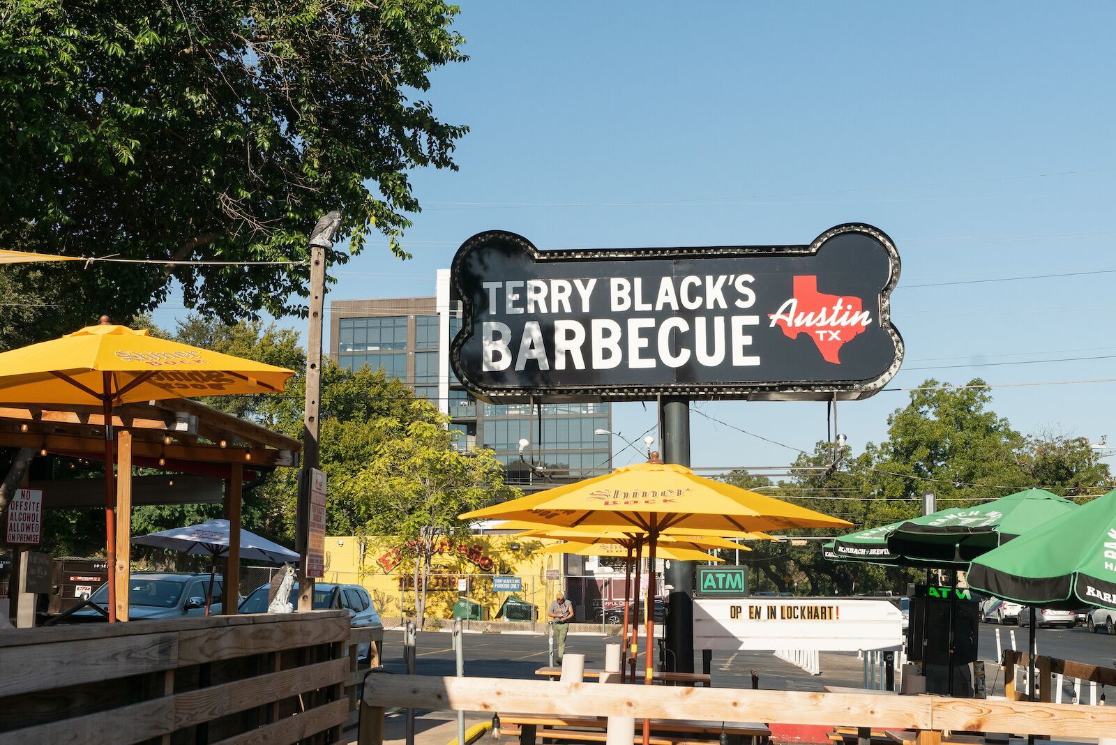 The exterior of Terry Black's Barbcue restaurant with black sign and yellow umbrellos