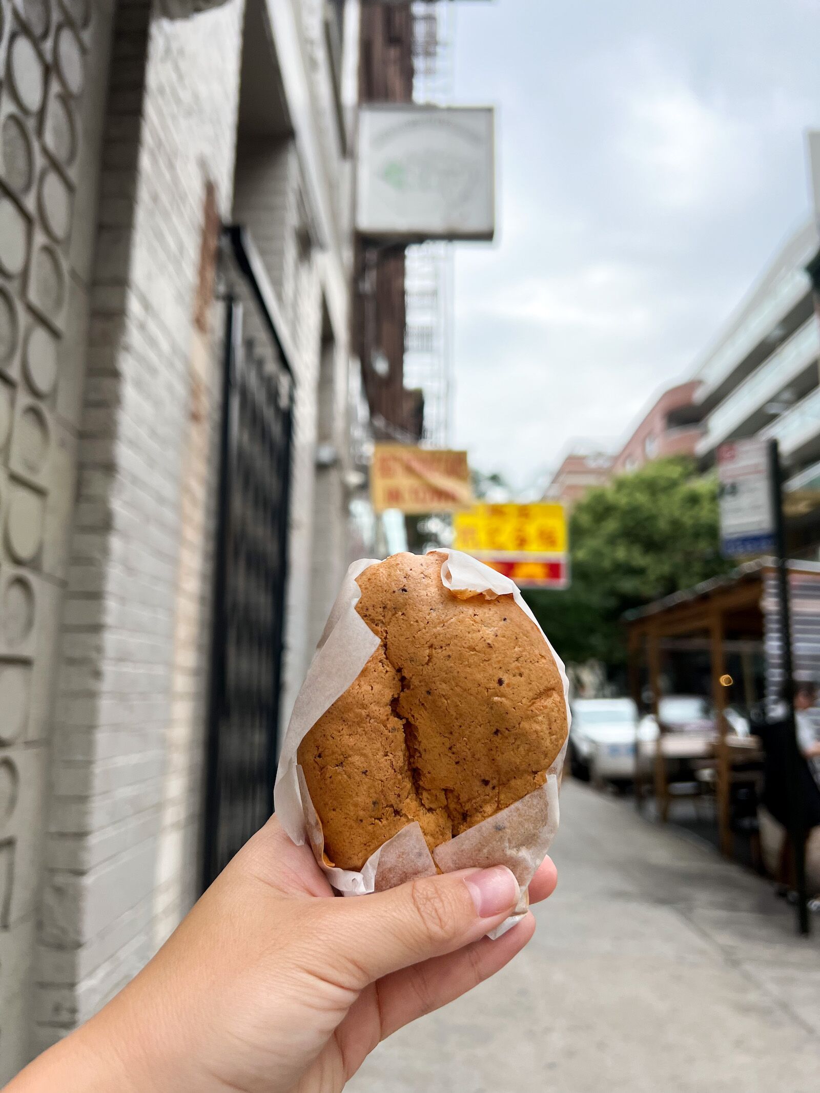 A woman's hand holds a sponge cake wrapped in paper from NYC Chinatown neighborhood bakery Kam Hing