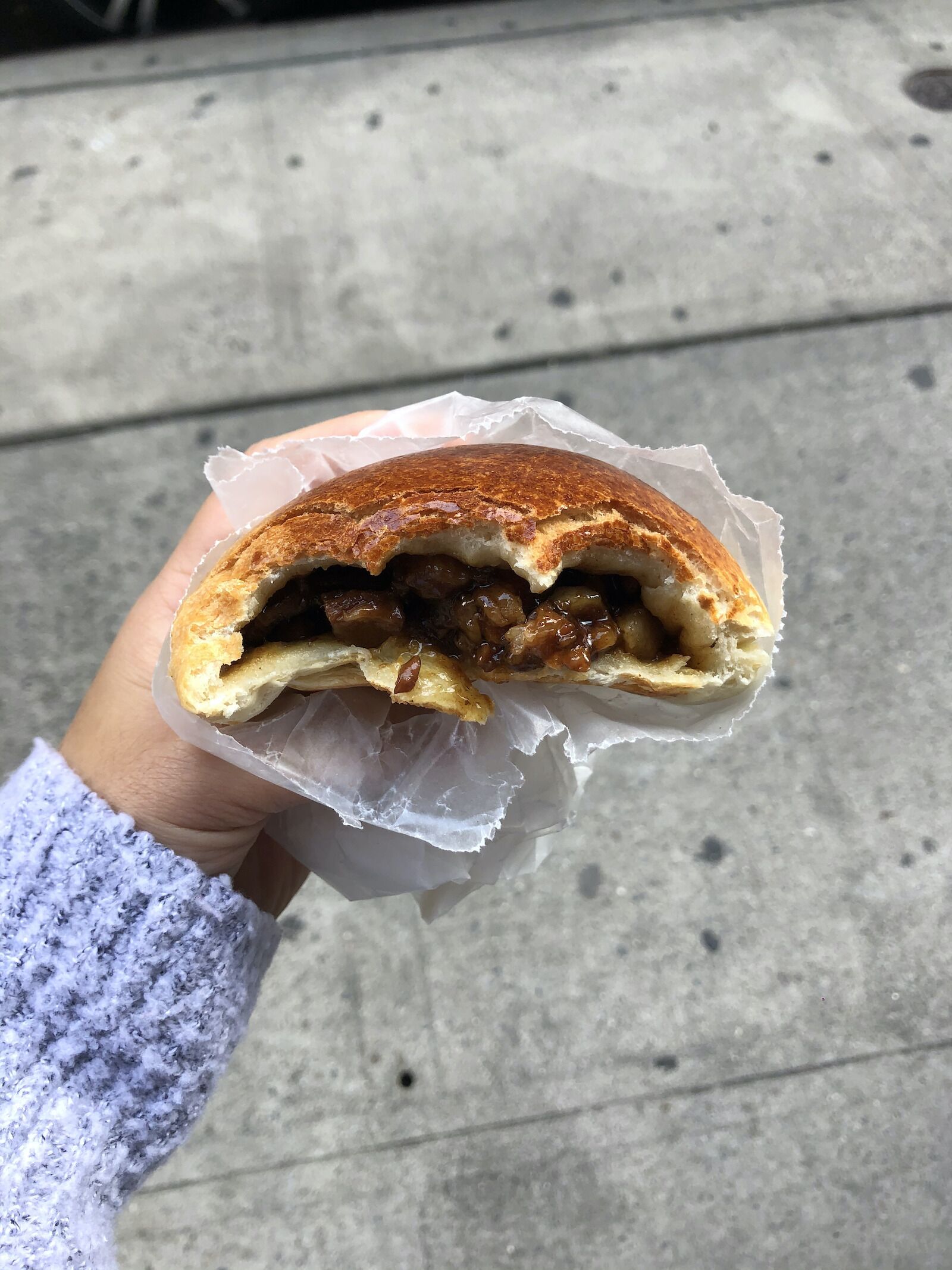 a woman's hand holding a barbecue pork bun with a bite taken out of it from NYC Chinatown neighborhood bakery Mei Lai Wah