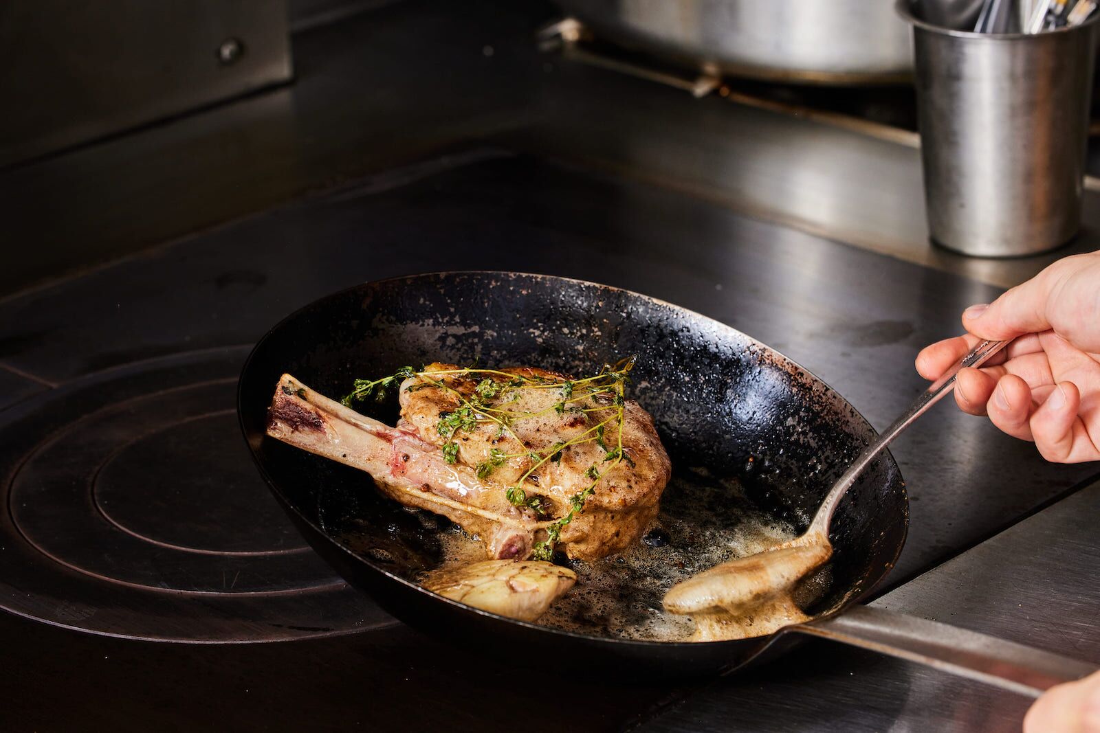 A lamb chop being cooked in a pan in the ktichen at L'Abeille, one of the most affordable Michelin star restaurants in New York City