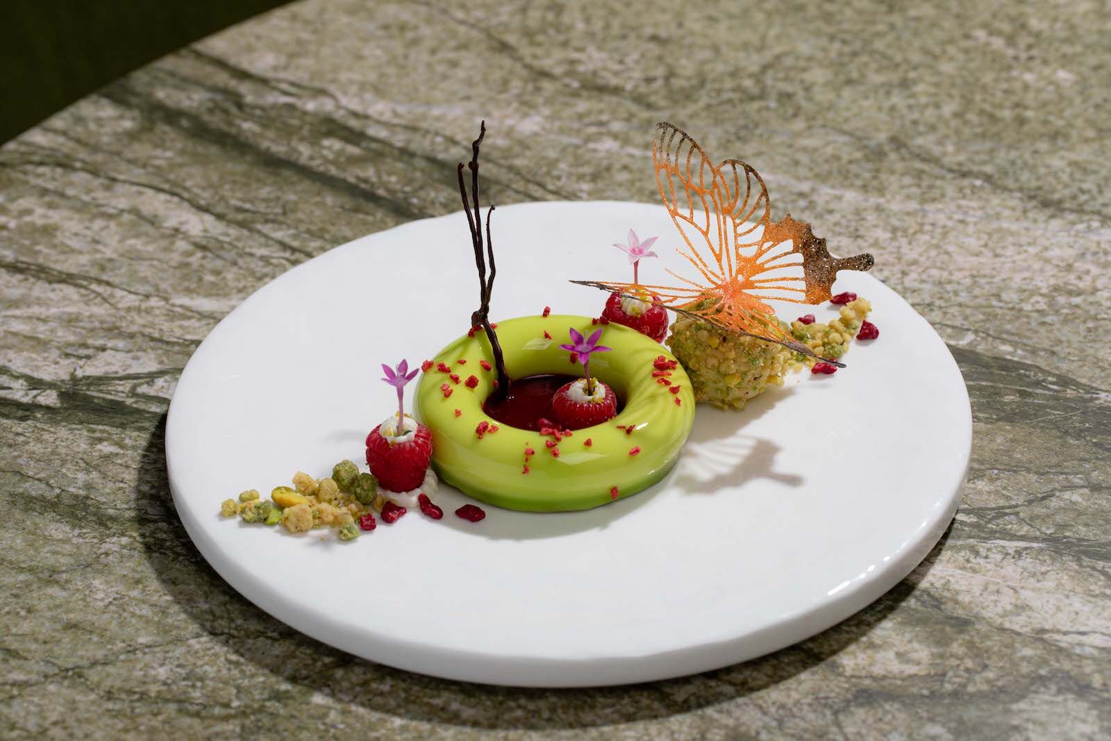 A green and red dish on a white plate on a wooden table that is served at La Jardinier, one of the most affordable Michelin star restaurants in New York City