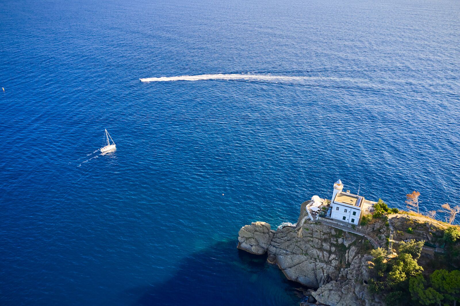 White yacht and motor boat are sailing near a light house in Portofino, Italy. A lighthouse is located on the hill near a seaside.