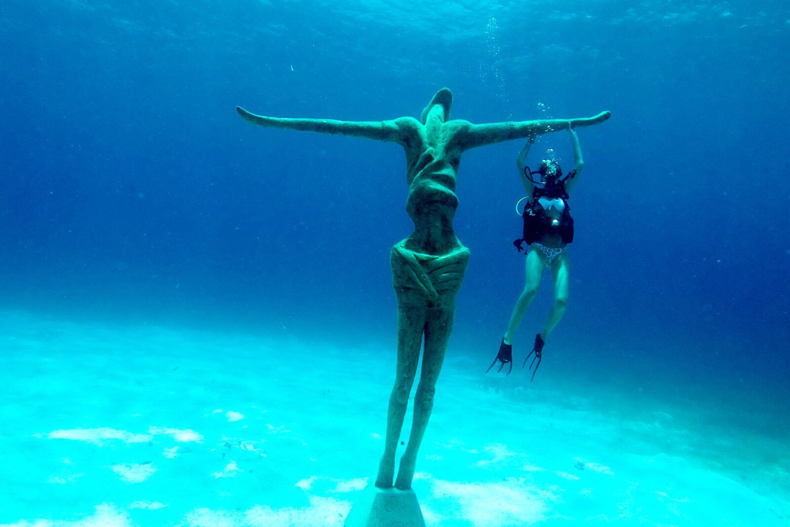 Woman scuba diving in canun underwater museum next to a statue