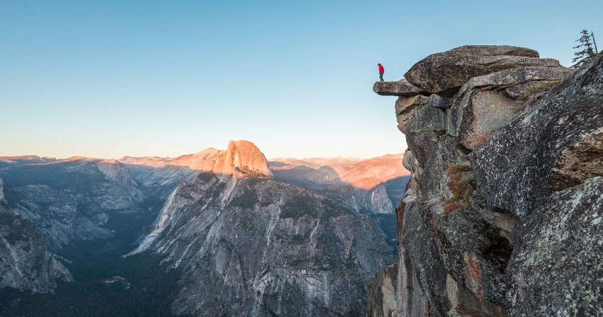 half dome hike yosemite, A fearless hiker is standing on an overhanging rock enjoying the view towards famous Half Dome at Glacier Point overlook in beautiful evening twilight, Yosemite National Park, California, USA