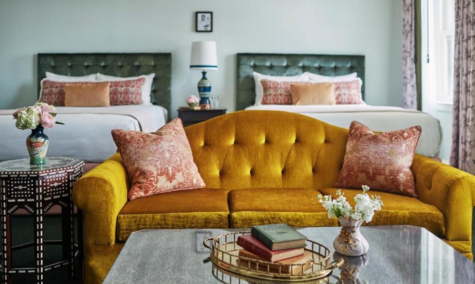 A yellow velvet couch in a room at the Pontchartrain Hotel with pink throw pillows and thwo beds in the background