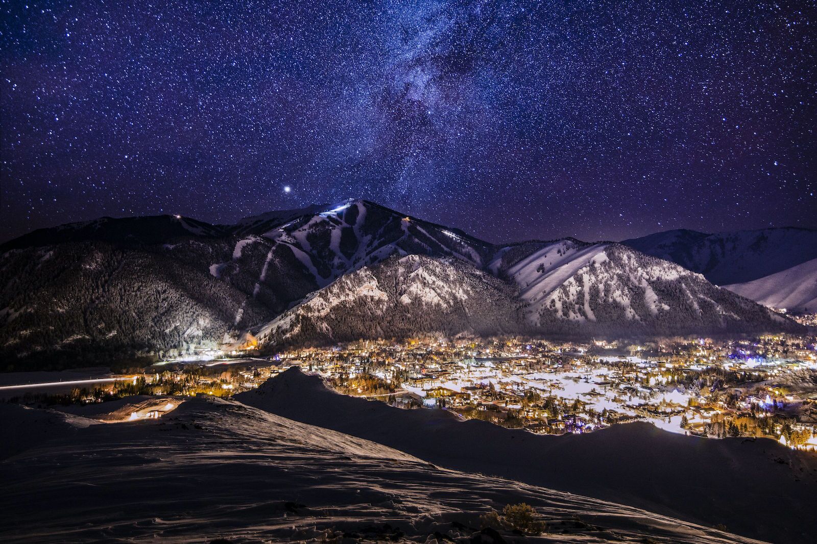 Sun Valley Idaho at night with clear sky, stars, mountains in the background, and the town lit up with lights