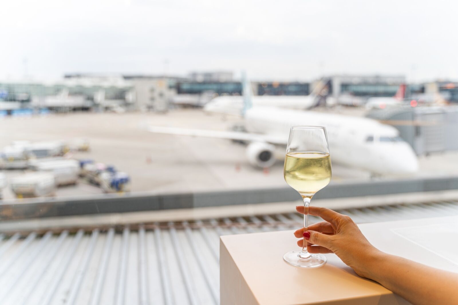 Female hand gently holding a glass of white wine in a cafe or restaurant with panoramic window with a view to an aircraft in an airport in Frankfurt