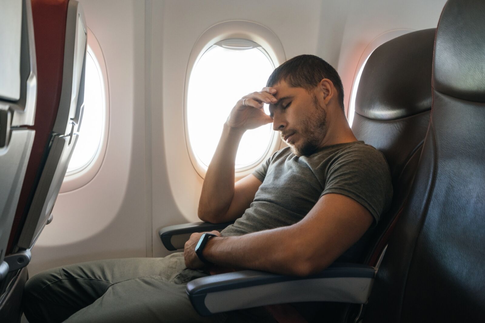man sleeps in an airplane while sitting in an armchair leaning on his arm.
