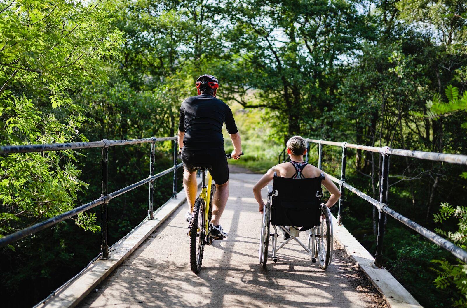 person in wheelchair and biker on bridge