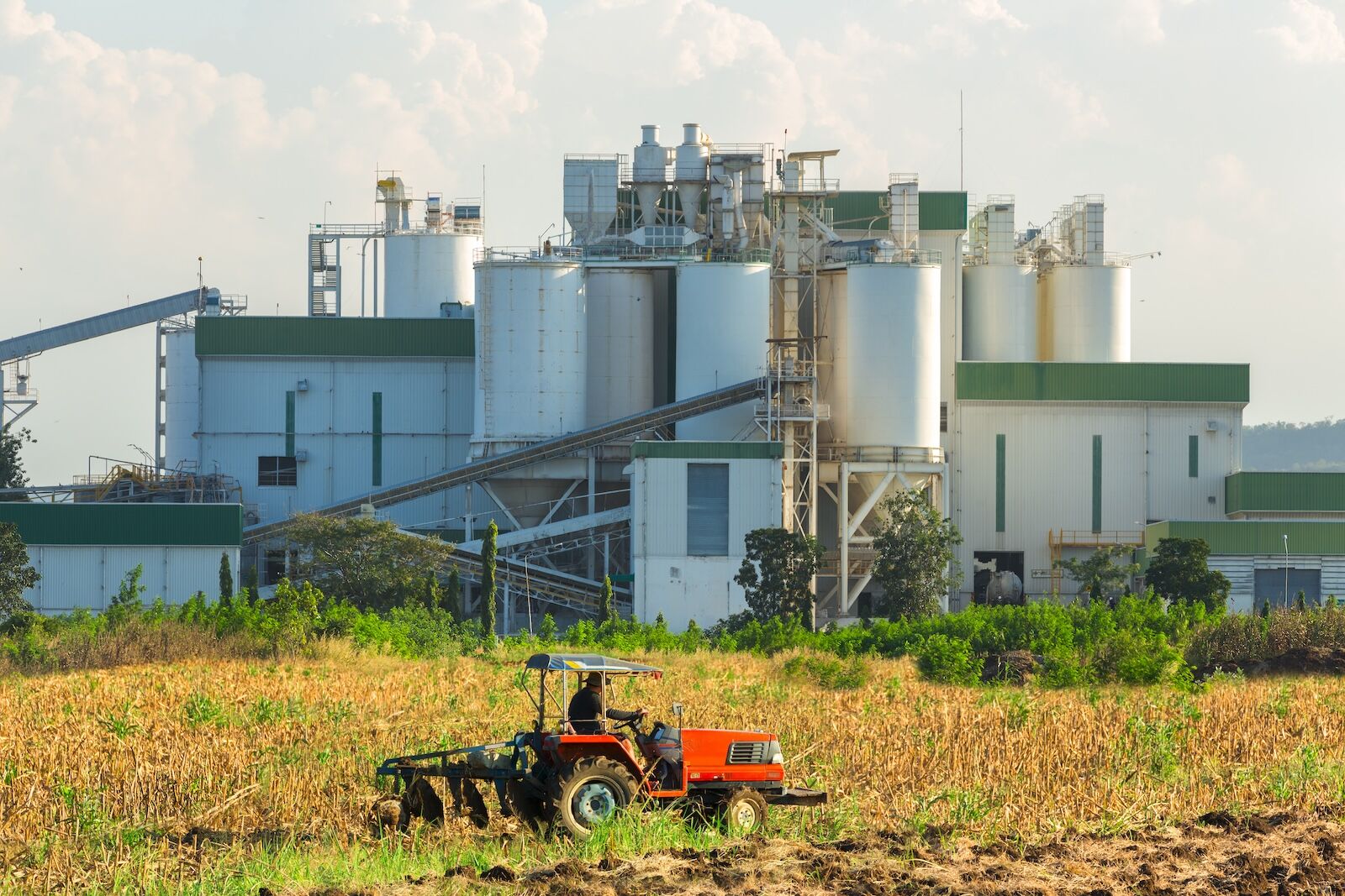man on tractor at corn farm in front of ethanol reginery