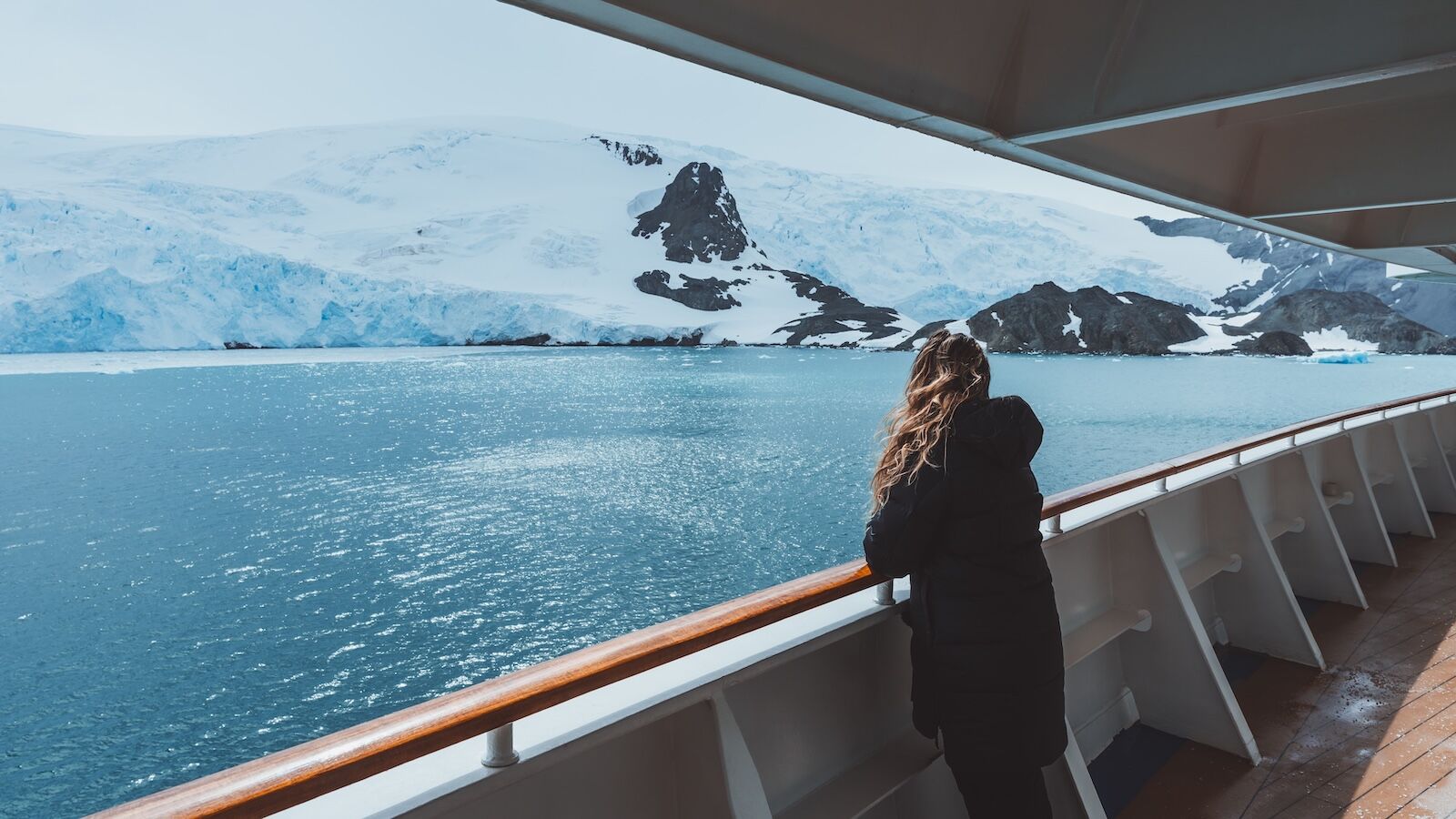 Antarctica Female Cruise Passenger Views Glacier. Beautiful Girl Hair Blowing in Wind on Side Railing Adventure Expedition Landscape Nature Wide Deck