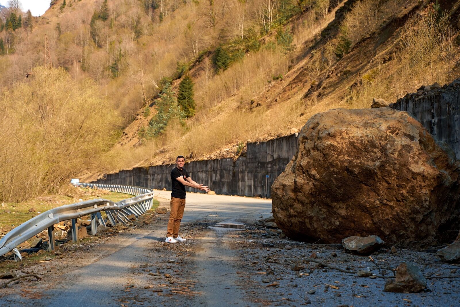 man standing next to giant boulder on road