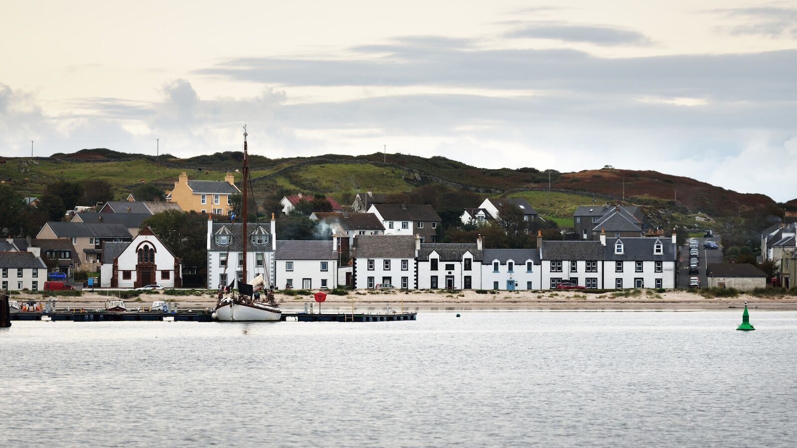 A view of the rocky shore of a small town Port Ellen at sunrise. Morning sunlight. Country houses, fishing boats and yachts close-up. Isle of Islay, Inner Hebrides, Scotland, UK