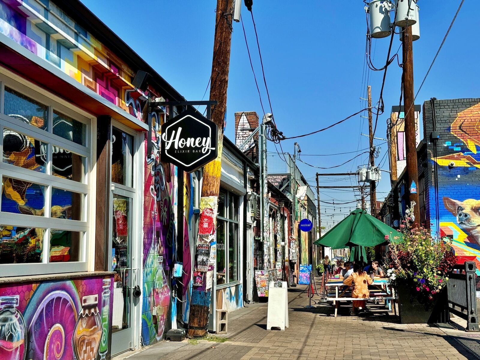 Denver, CO, USA - Oct 1, 2024: Colorful alley in the RiNo Art District with Honey Elixir Bar, street art, overhead cables, outdoor dining tables, and a mural-covered walkway in a vibrant urban setting